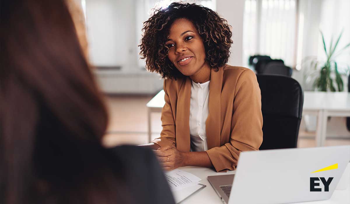 2 women sitting at a desk with a laptop on the foreground